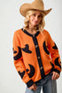 Woman wearing an orange sweater with black witch hat patterns and a cowboy hat.
