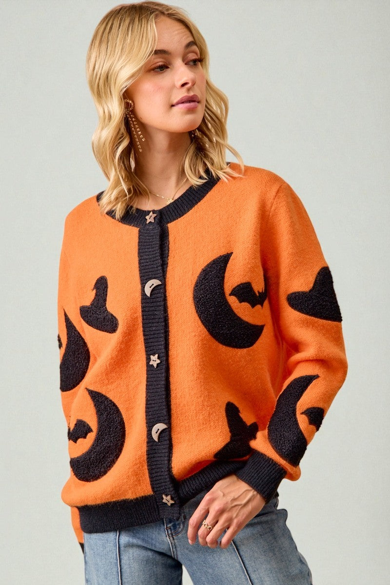 Woman wearing an orange cardigan with black cat patterns on a plain background