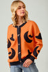 Woman wearing an orange cardigan with black cat patterns on a plain background