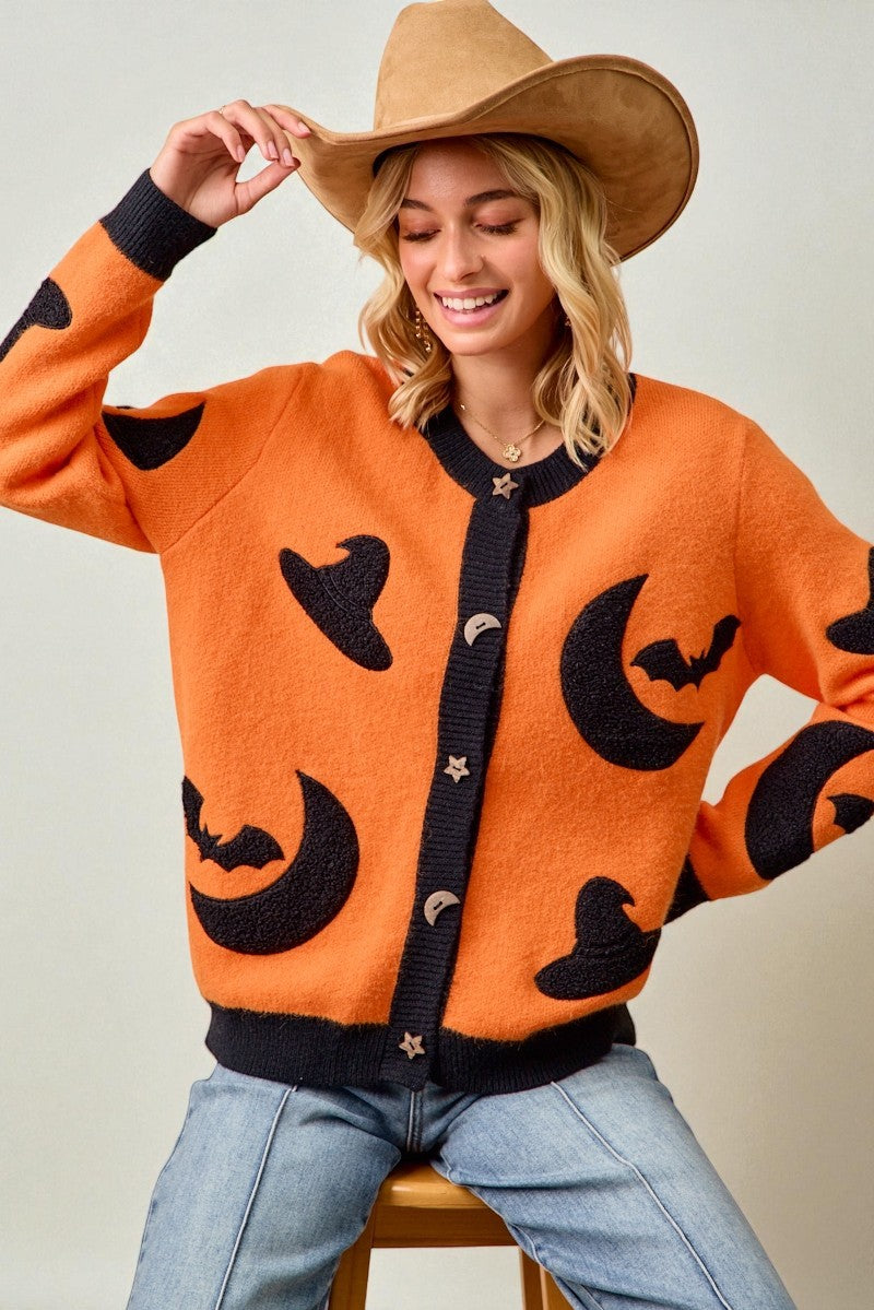 Woman wearing an orange sweater with black Halloween patterns, sitting on a chair.
