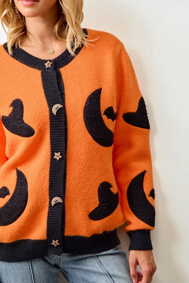 Person wearing an orange cardigan with black moon and star patterns on a white background