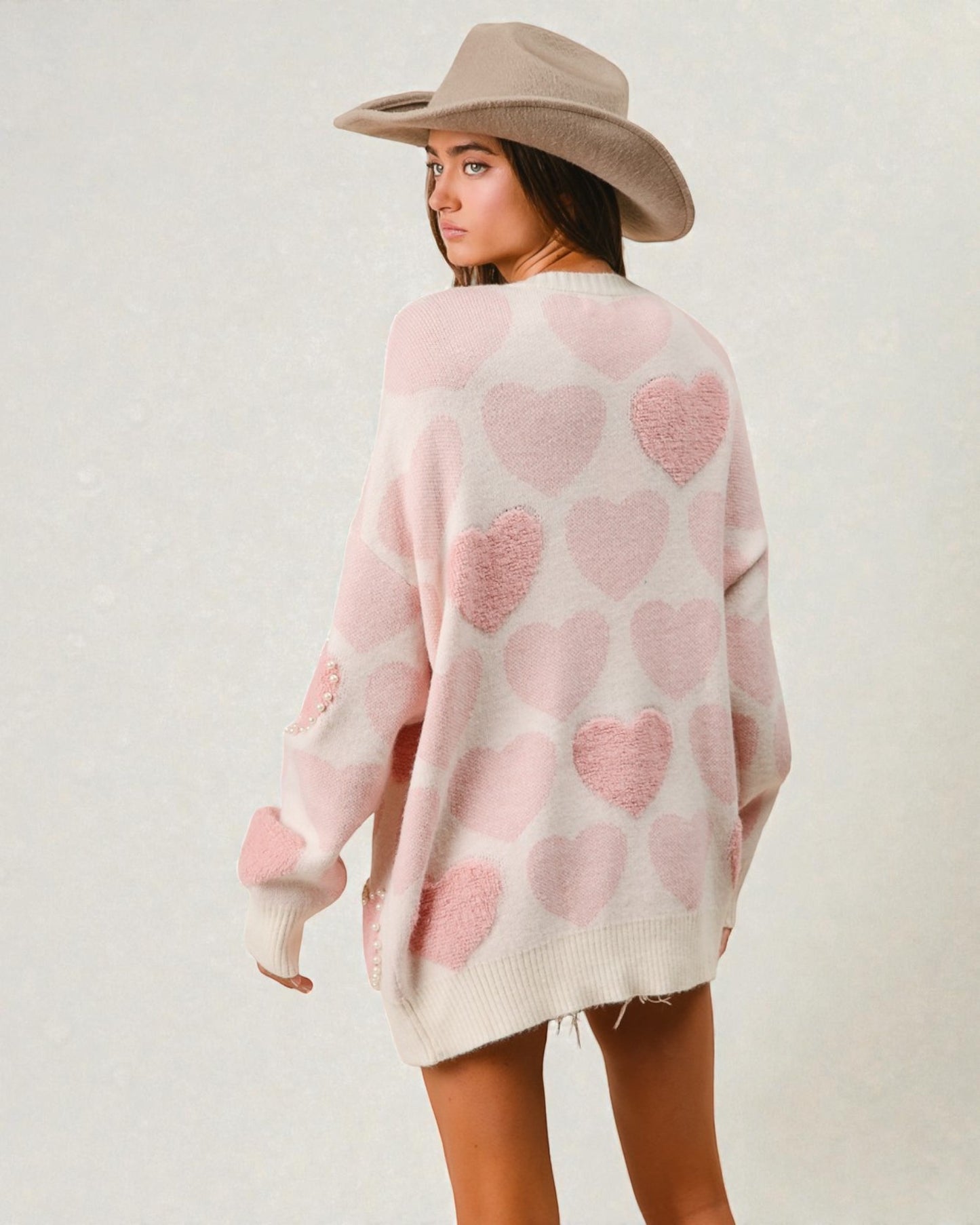 Woman wearing a pink heart-patterned sweater and beige hat on a plain background