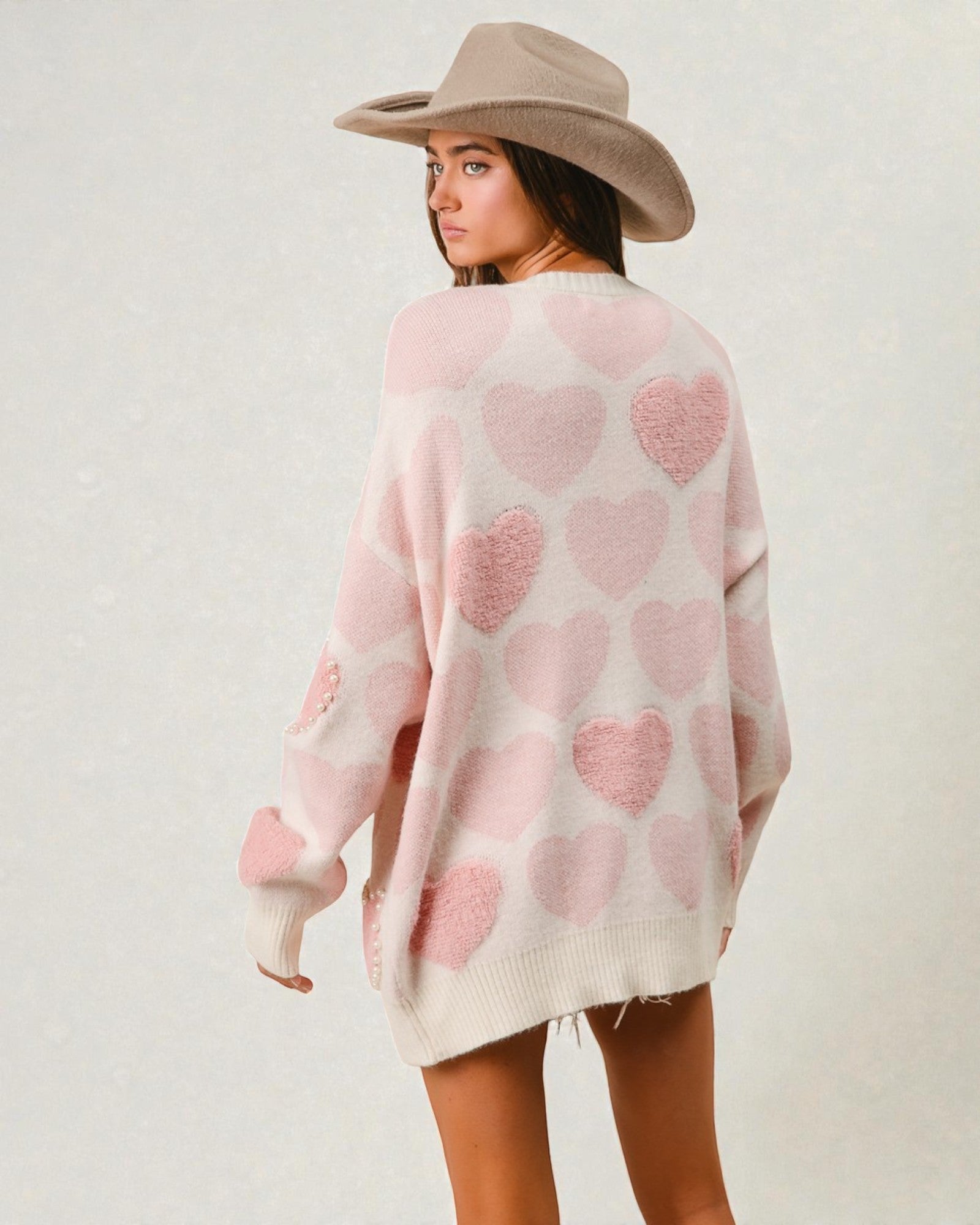 Woman wearing a pink heart-patterned sweater and beige hat on a plain background