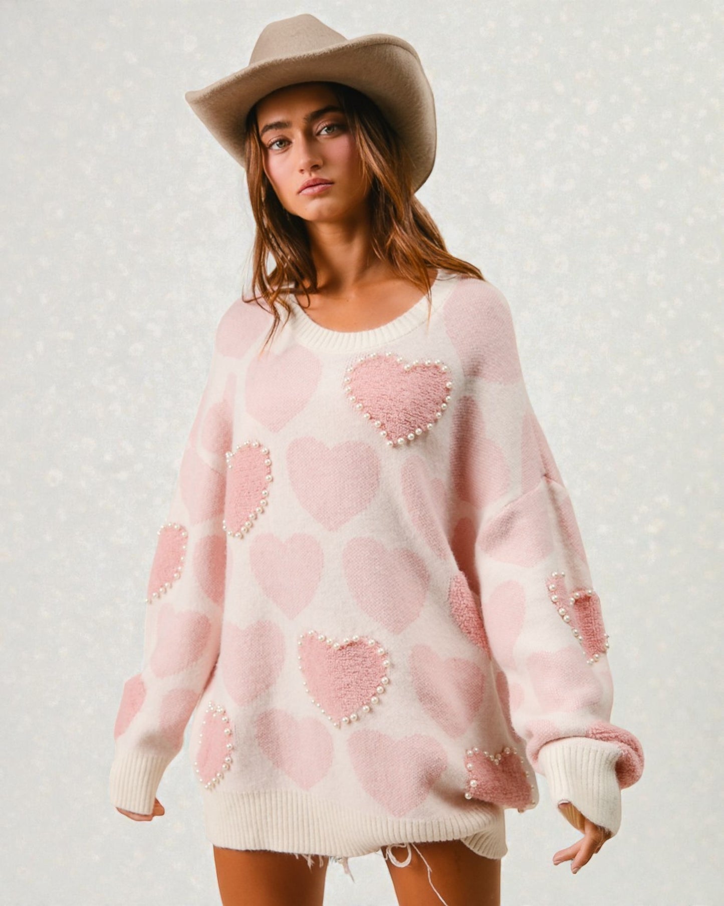 Woman wearing a pink sweater with heart patterns and a beige hat against a light background