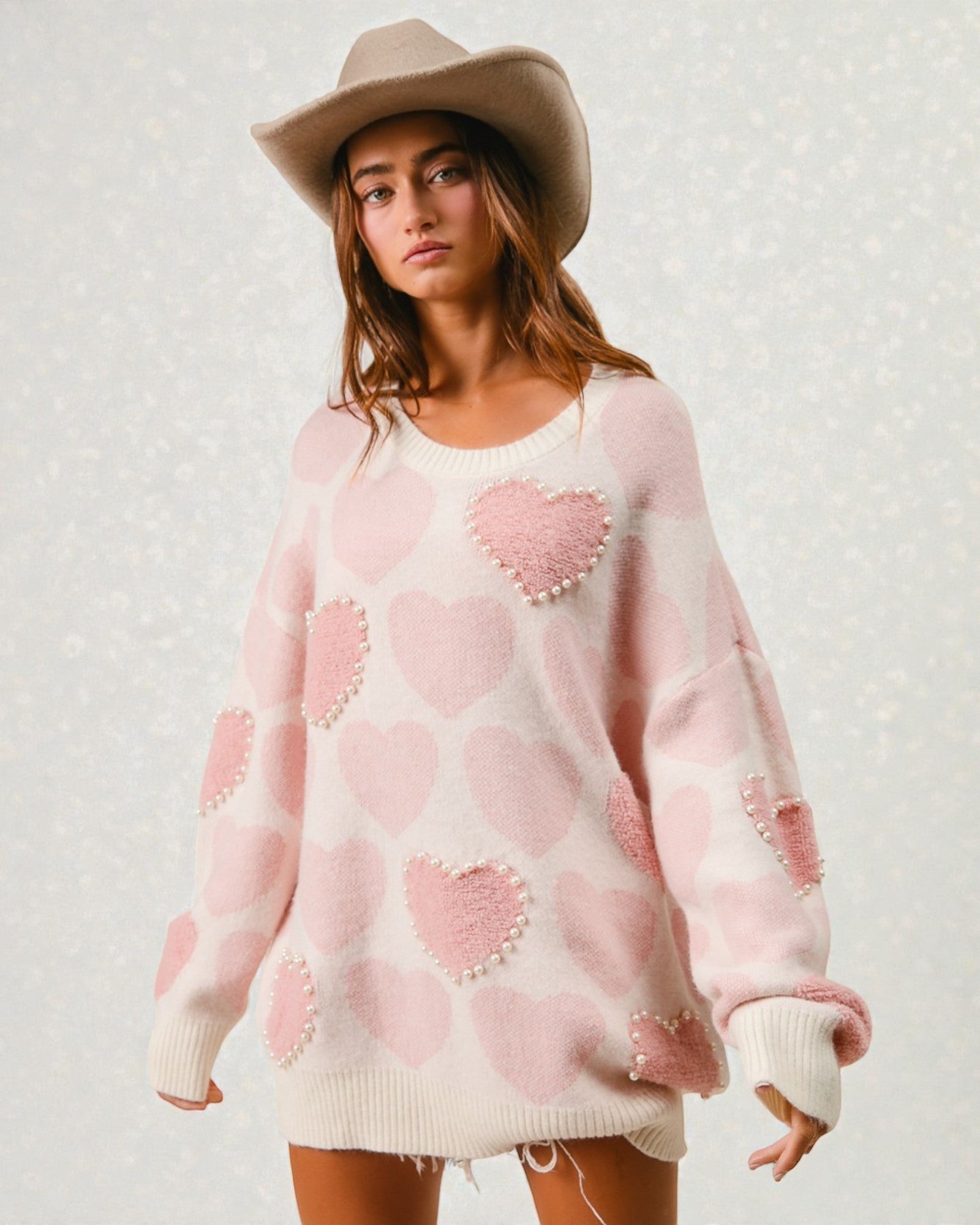 Woman wearing a pink sweater with heart patterns and a beige hat against a light background
