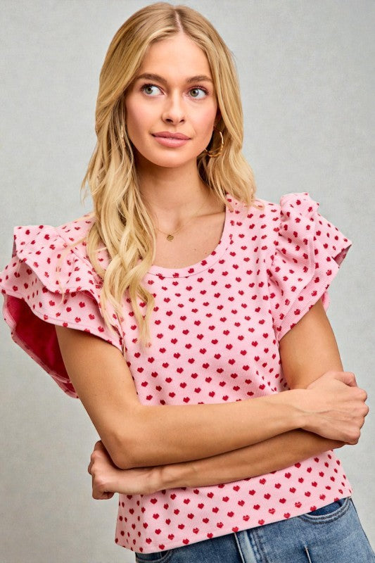 Woman wearing a pink top with red heart patterns against a gray background