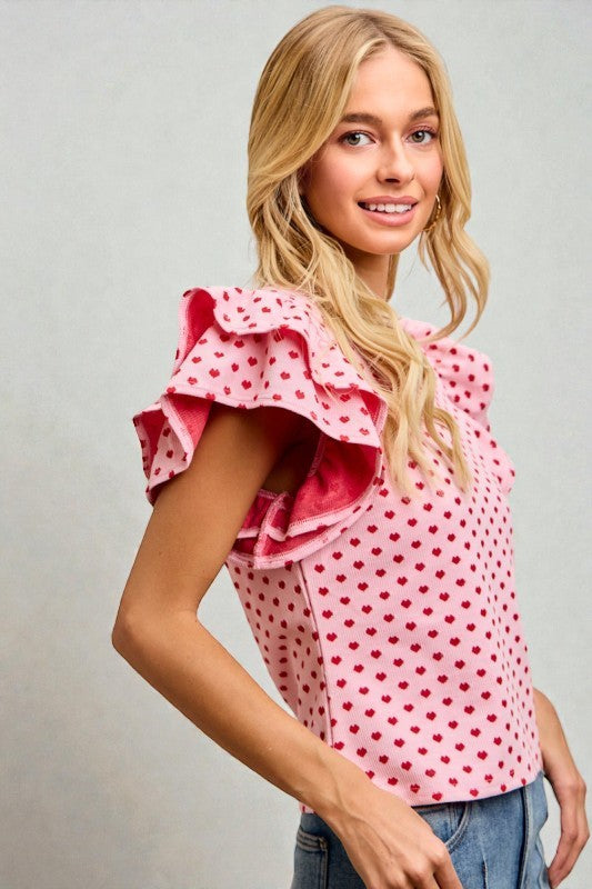 Woman wearing a pink blouse with red polka dots and ruffled sleeves against a gray background