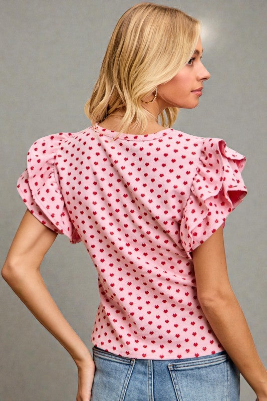 Woman wearing a pink polka dot blouse with ruffled sleeves against a gray background