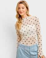 Woman wearing a beige long-sleeve top with black polka dots and light blue jeans on a white background