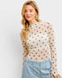 Woman wearing a beige long-sleeve top with black polka dots and light blue jeans on a white background