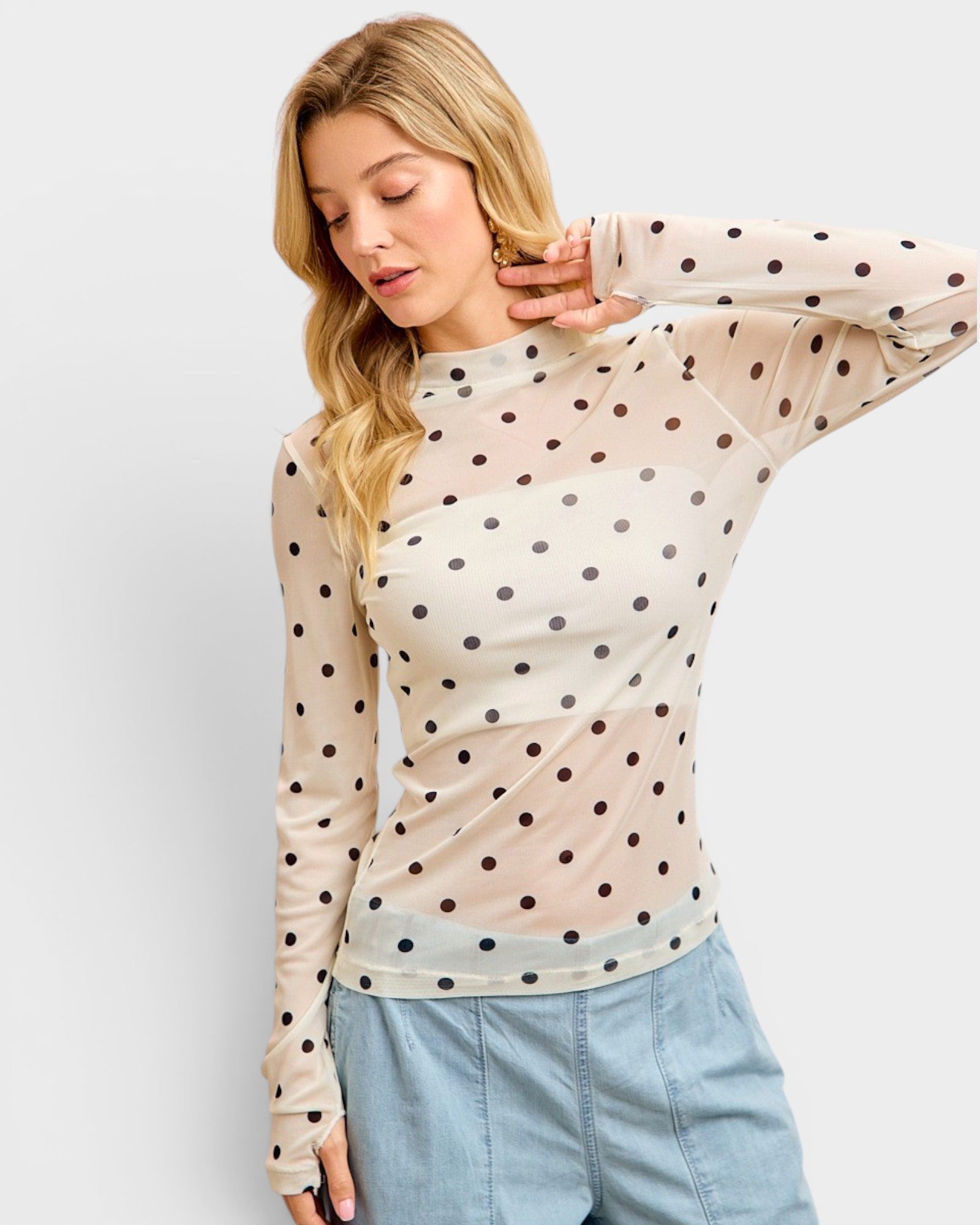 Woman wearing a beige long-sleeve top with black polka dots and light blue jeans on a white background