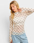 Woman wearing a beige long-sleeve top with black polka dots and light blue jeans on a white background