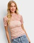 Woman wearing a pink lace top and jeans against a light background