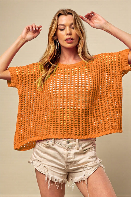 Woman wearing an orange crochet top and beige shorts against a beige background