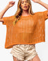 A woman wearing a loose, short-sleeve orange crochet knit top and light beige frayed denim shorts, posing against a plain white background.
