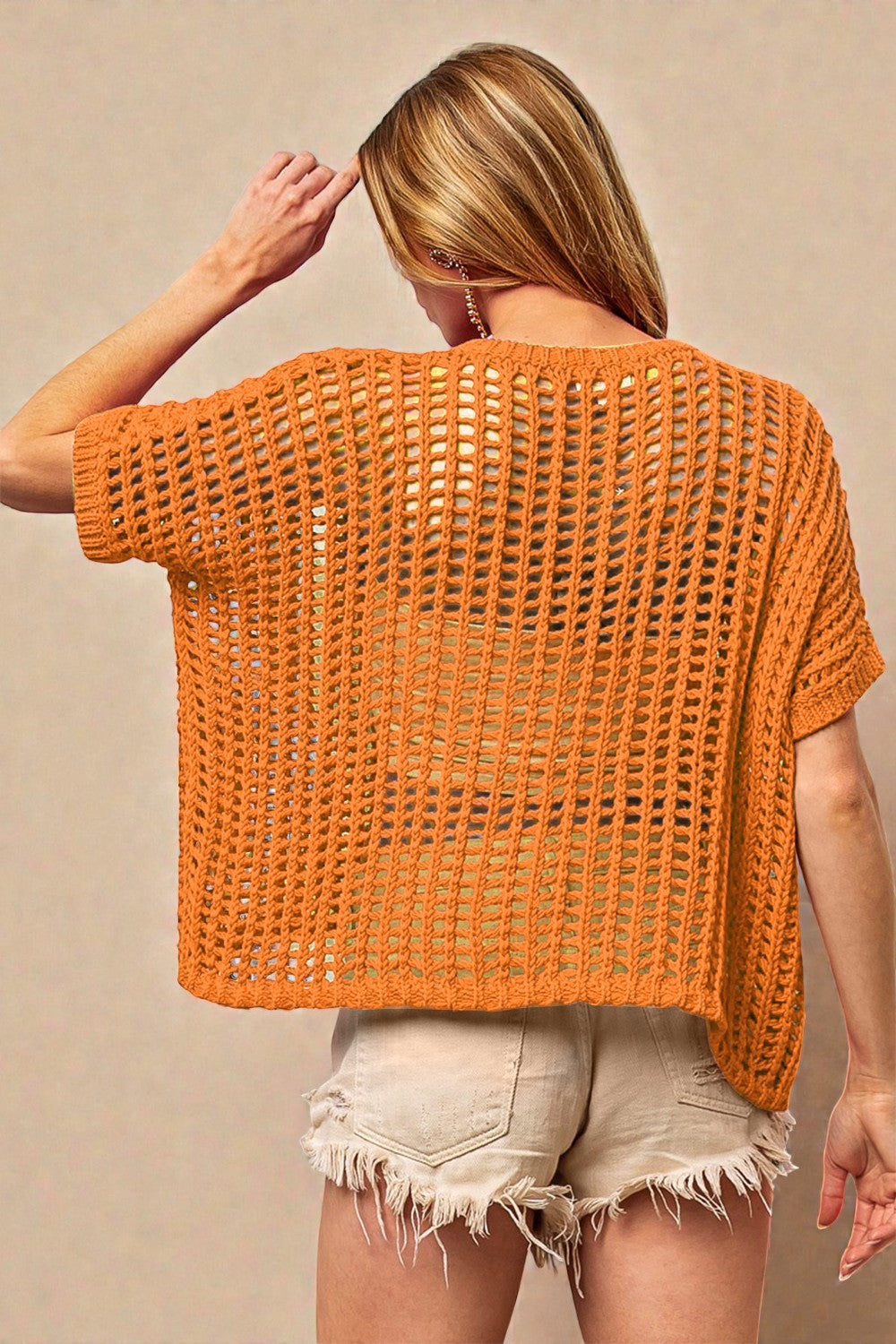 Woman wearing an orange crochet top against a beige background