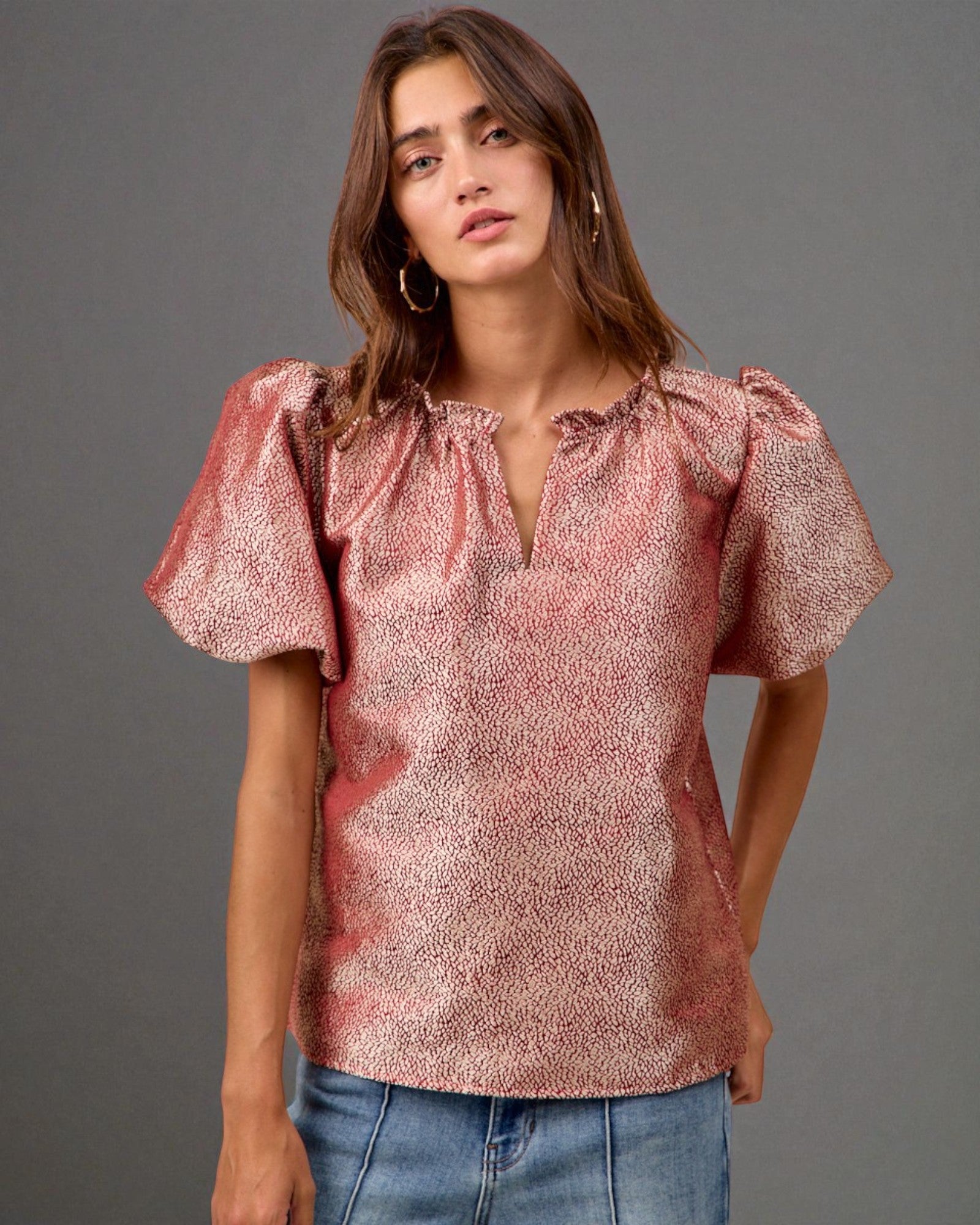 Woman wearing a pink blouse with ruffled sleeves against a gray background