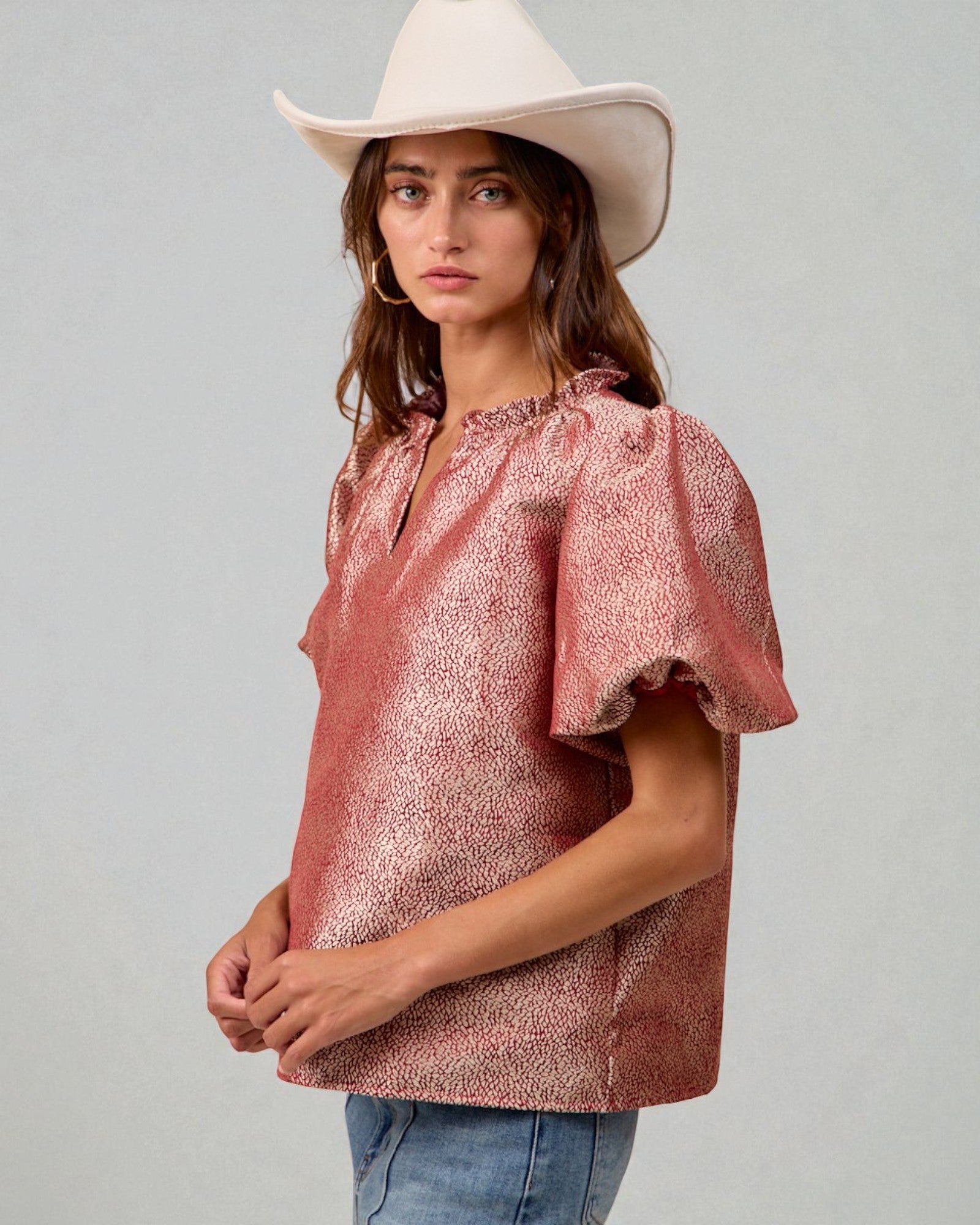 Woman wearing a pink metallic blouse and white hat against a gray background