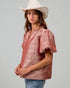Woman wearing a pink metallic blouse and white hat against a gray background