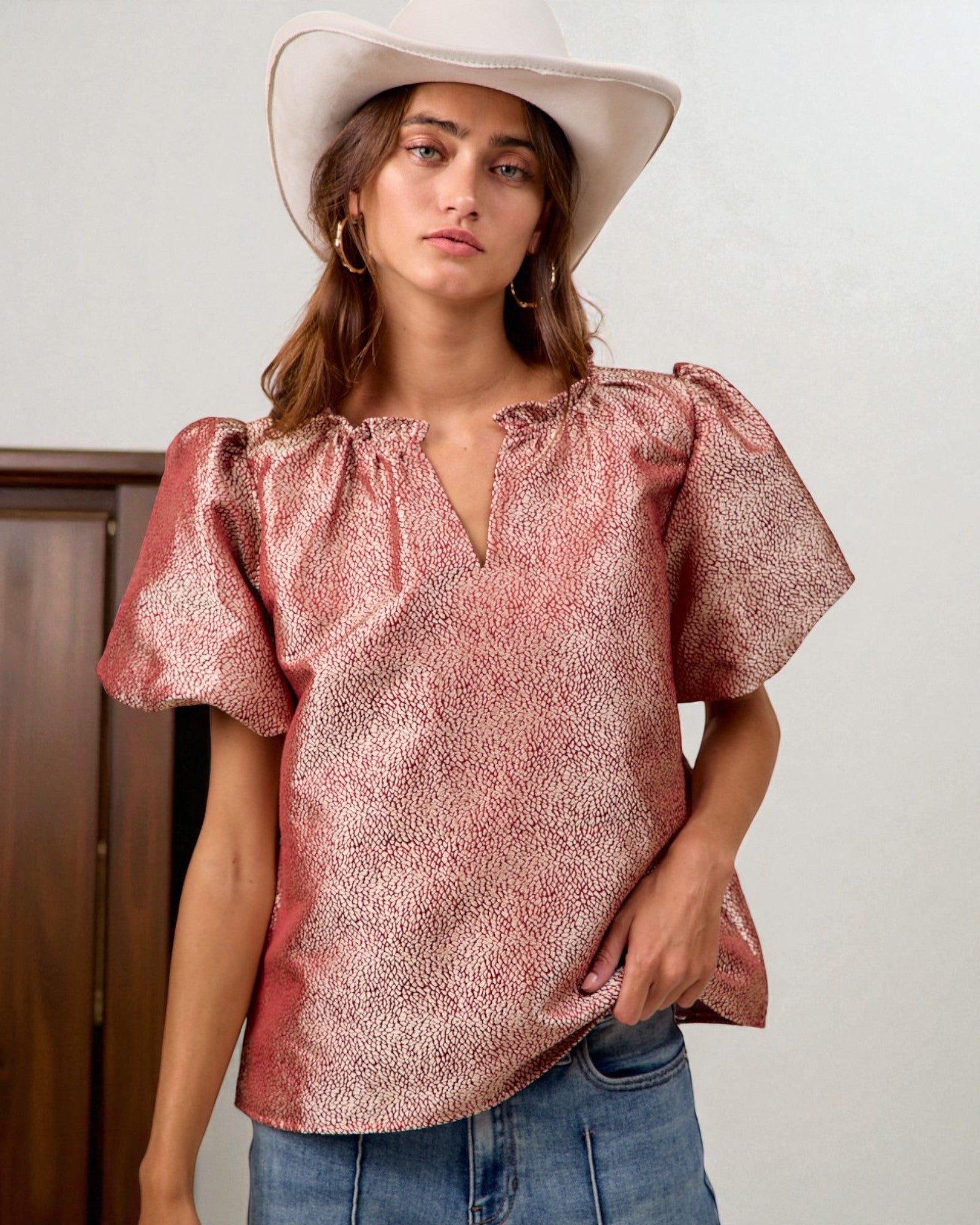 Woman wearing a pink metallic blouse and white hat against a plain background