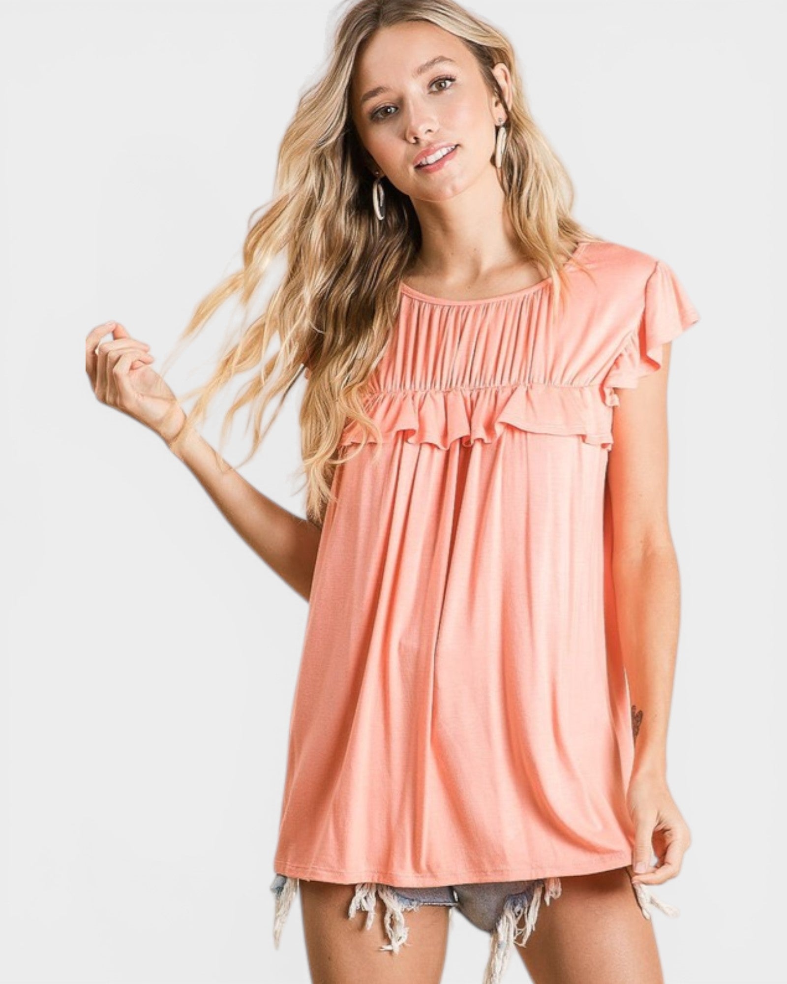 Woman wearing a peach-colored top with ruffled sleeves on a white background