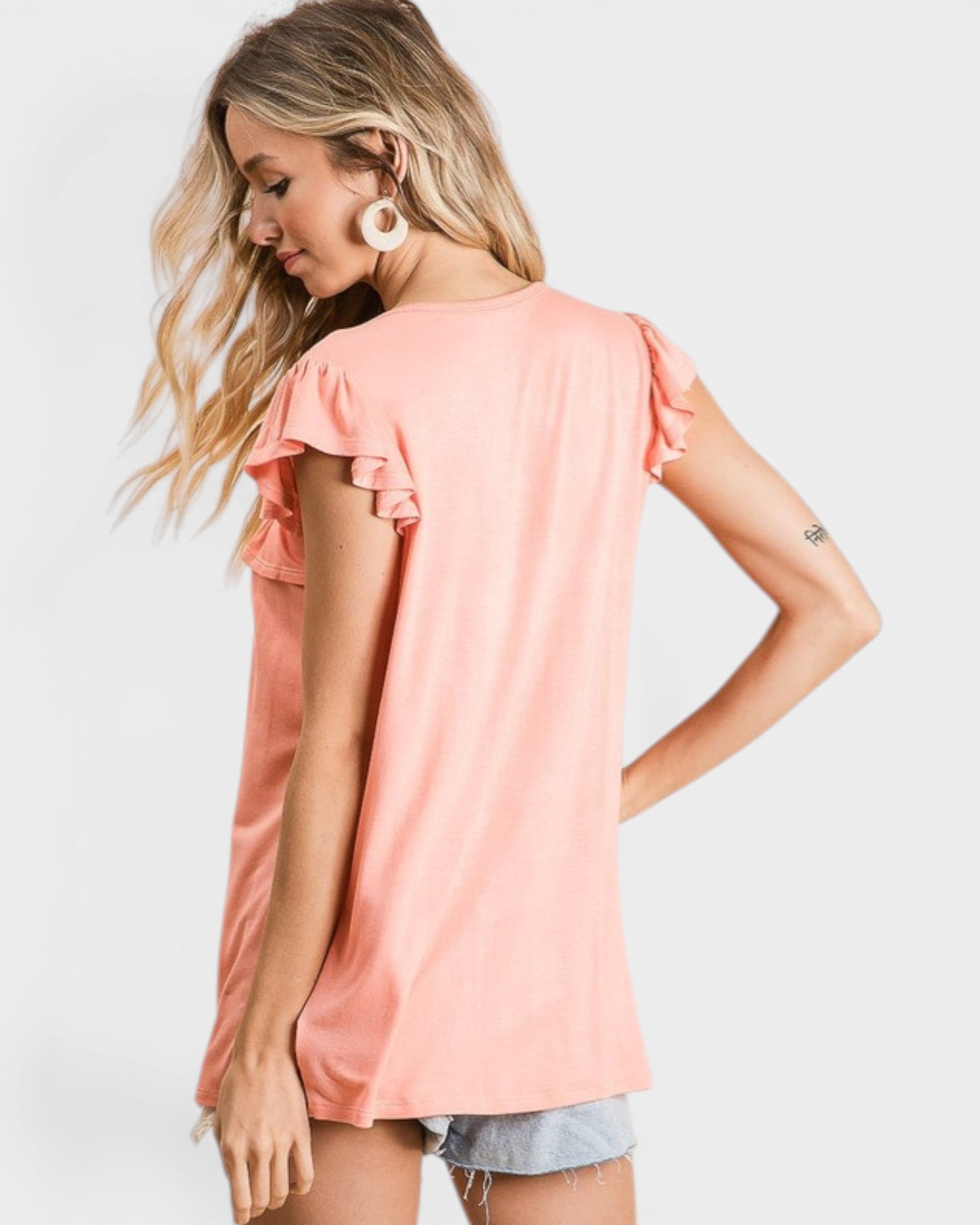Woman wearing a peach-colored top with ruffled sleeves on a white background