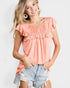Woman wearing a peach ruffled top and denim shorts on a white background