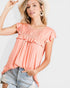 Woman wearing a coral ruffled top and denim shorts on a white background