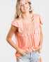 Woman wearing a peach-colored ruffled top with a plain background