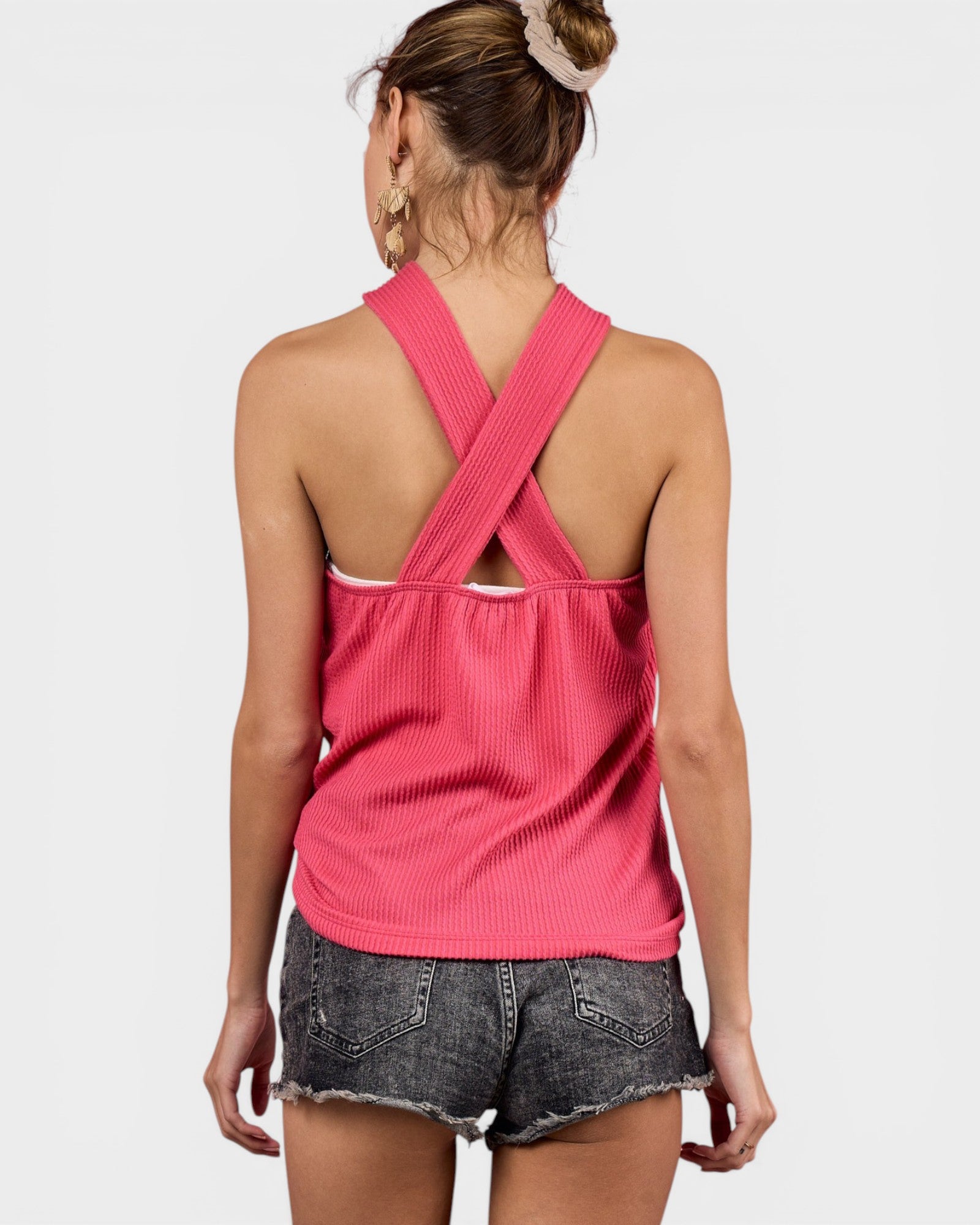 Woman wearing a pink ribbed tank top with crossed back design on a white background