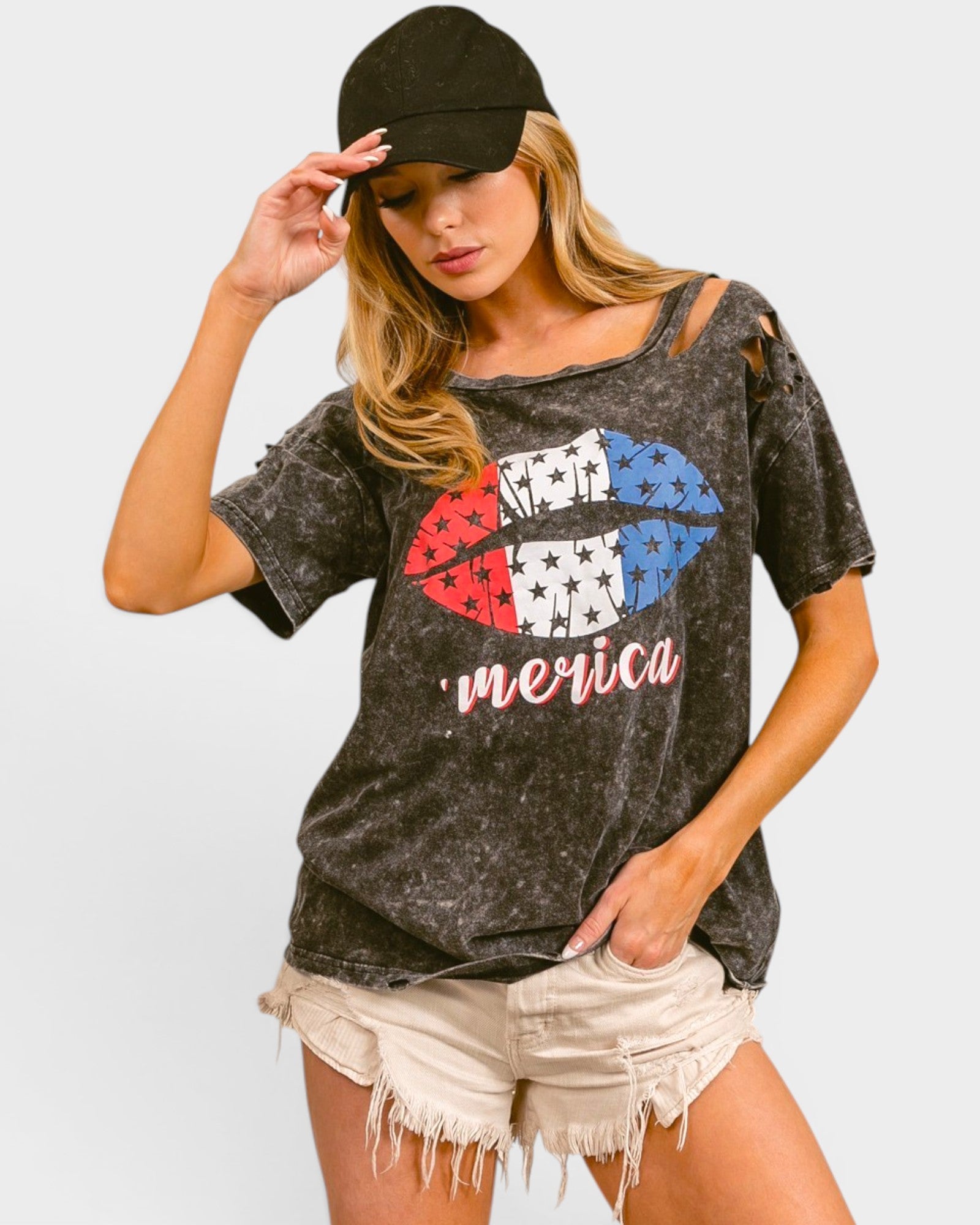 Woman wearing a graphic t-shirt with 'Merica' design and a cap on a light gray background