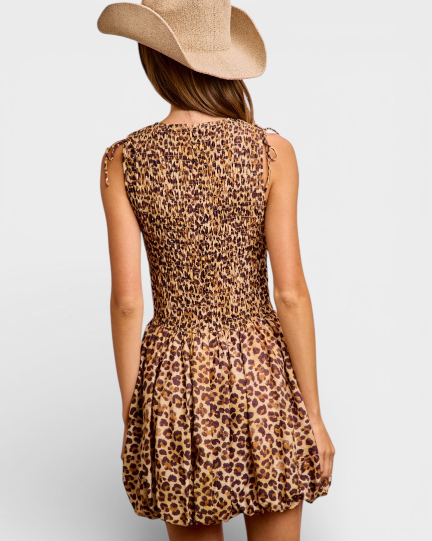 Person wearing a leopard print dress and cowboy hat on a plain background