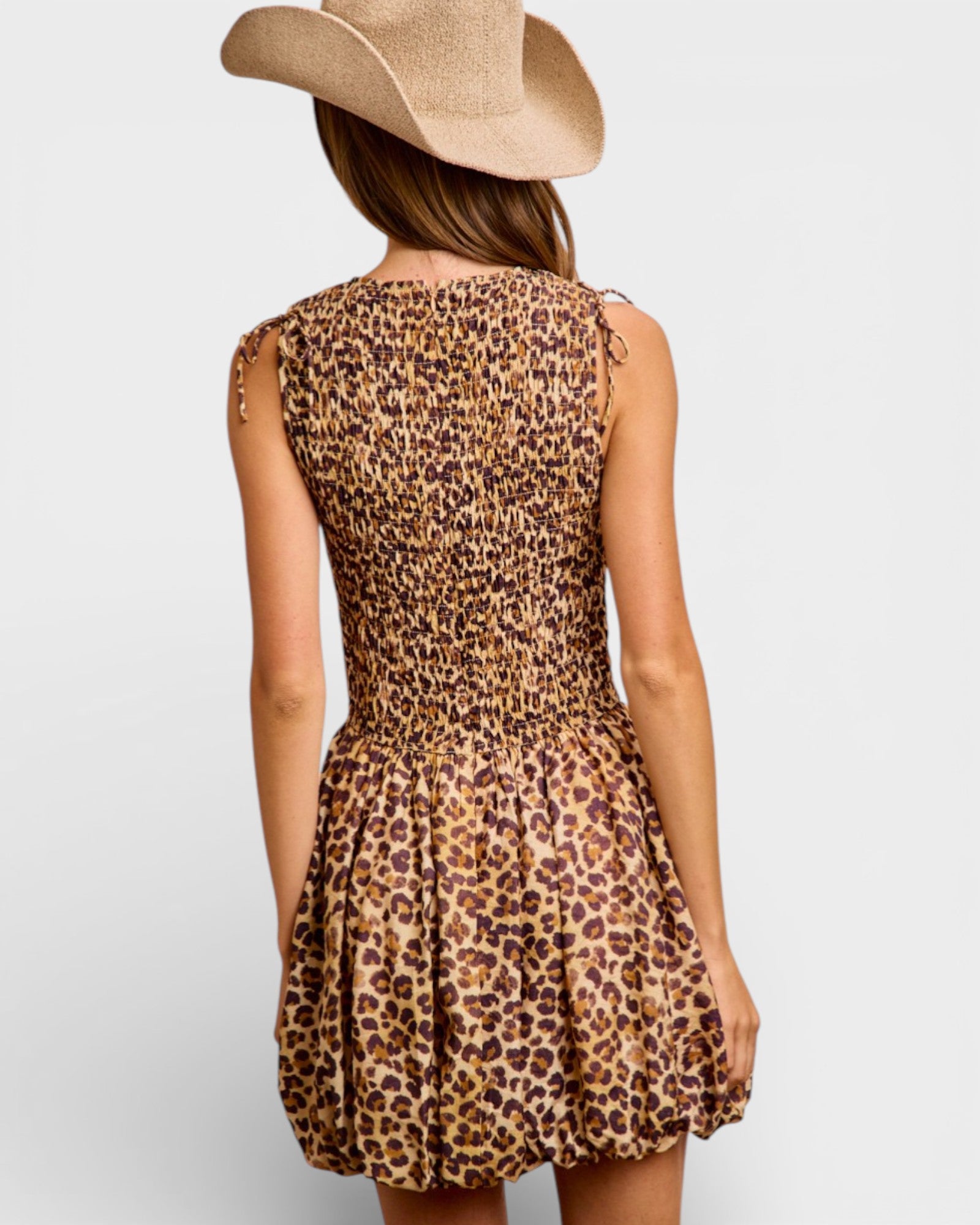 Person wearing a leopard print dress and cowboy hat on a plain background