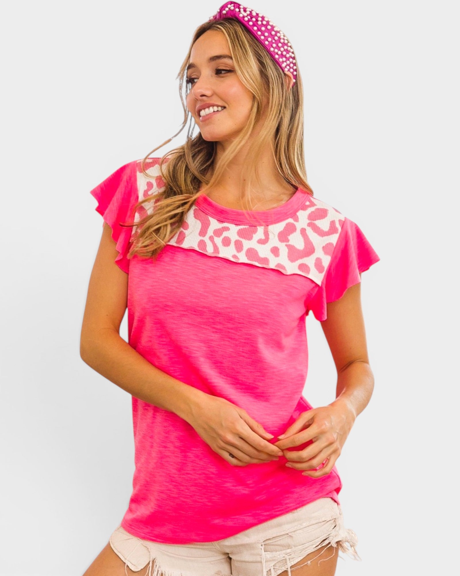 Woman wearing a bright pink top with leopard print trim and a matching headband on a white background