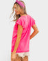 Woman wearing a bright pink t-shirt and white shorts on a plain background
