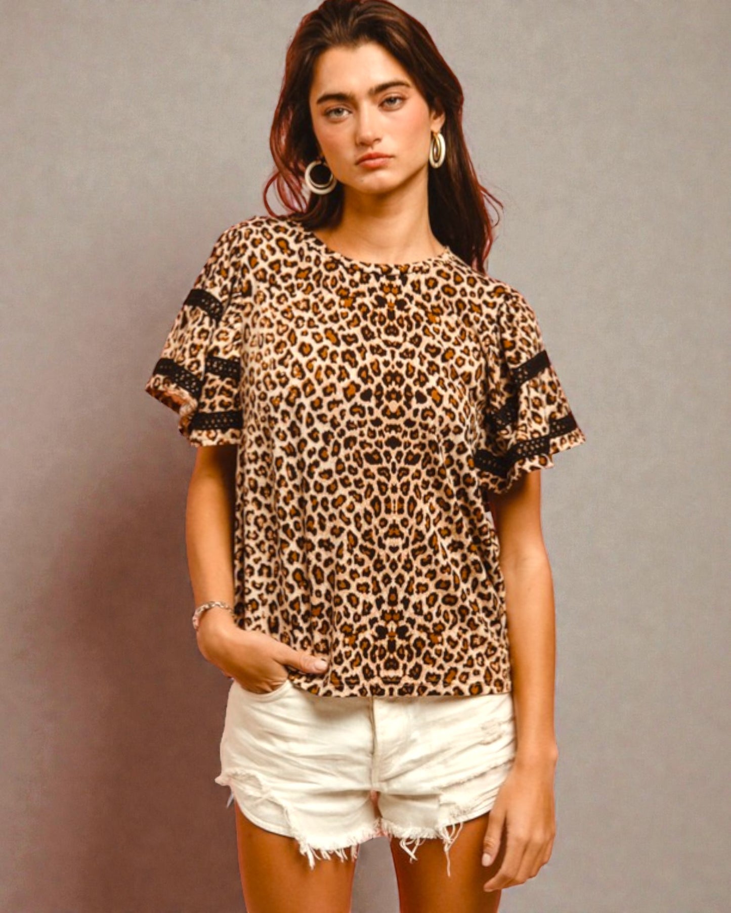Woman wearing a leopard print top with black lace sleeves against a gray background