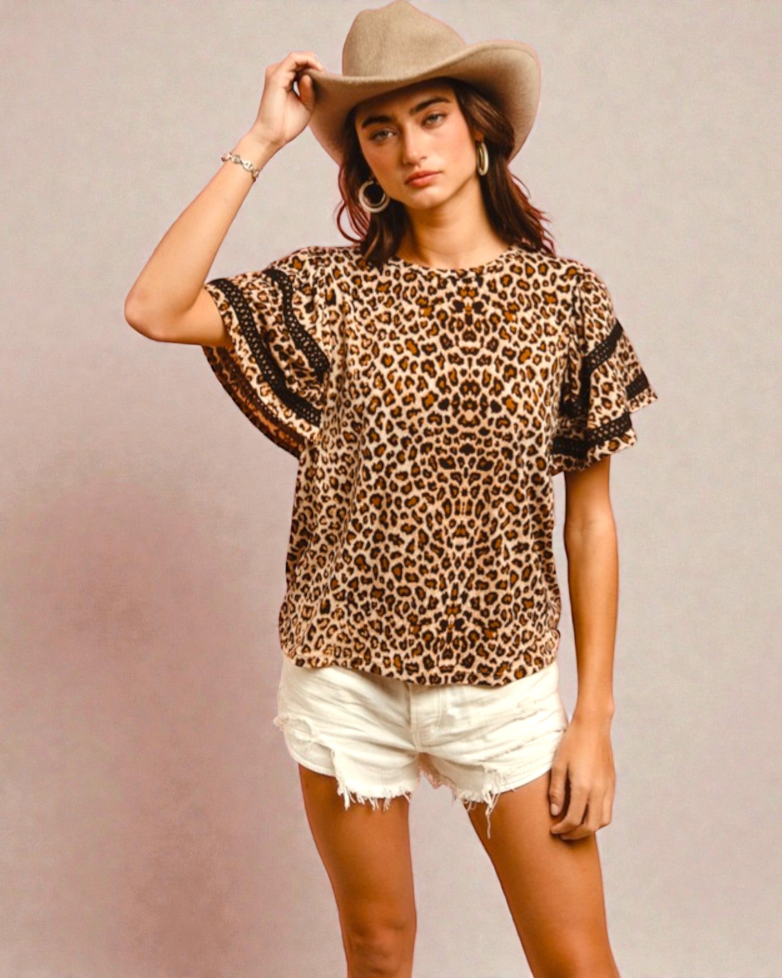 Woman wearing a leopard print top with ruffled sleeves and white shorts against a plain background