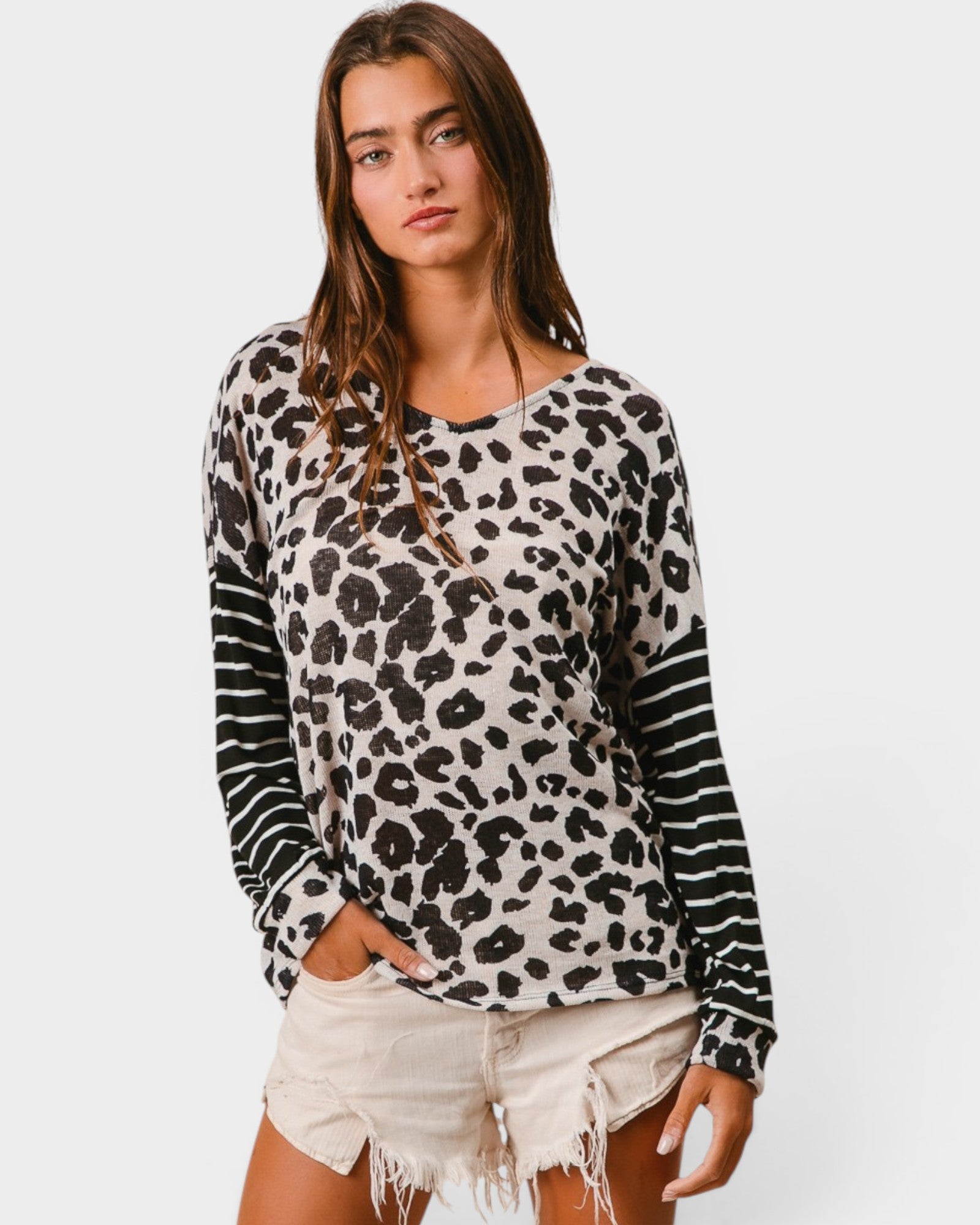 Woman wearing a leopard print long-sleeve top and white shorts on a plain background