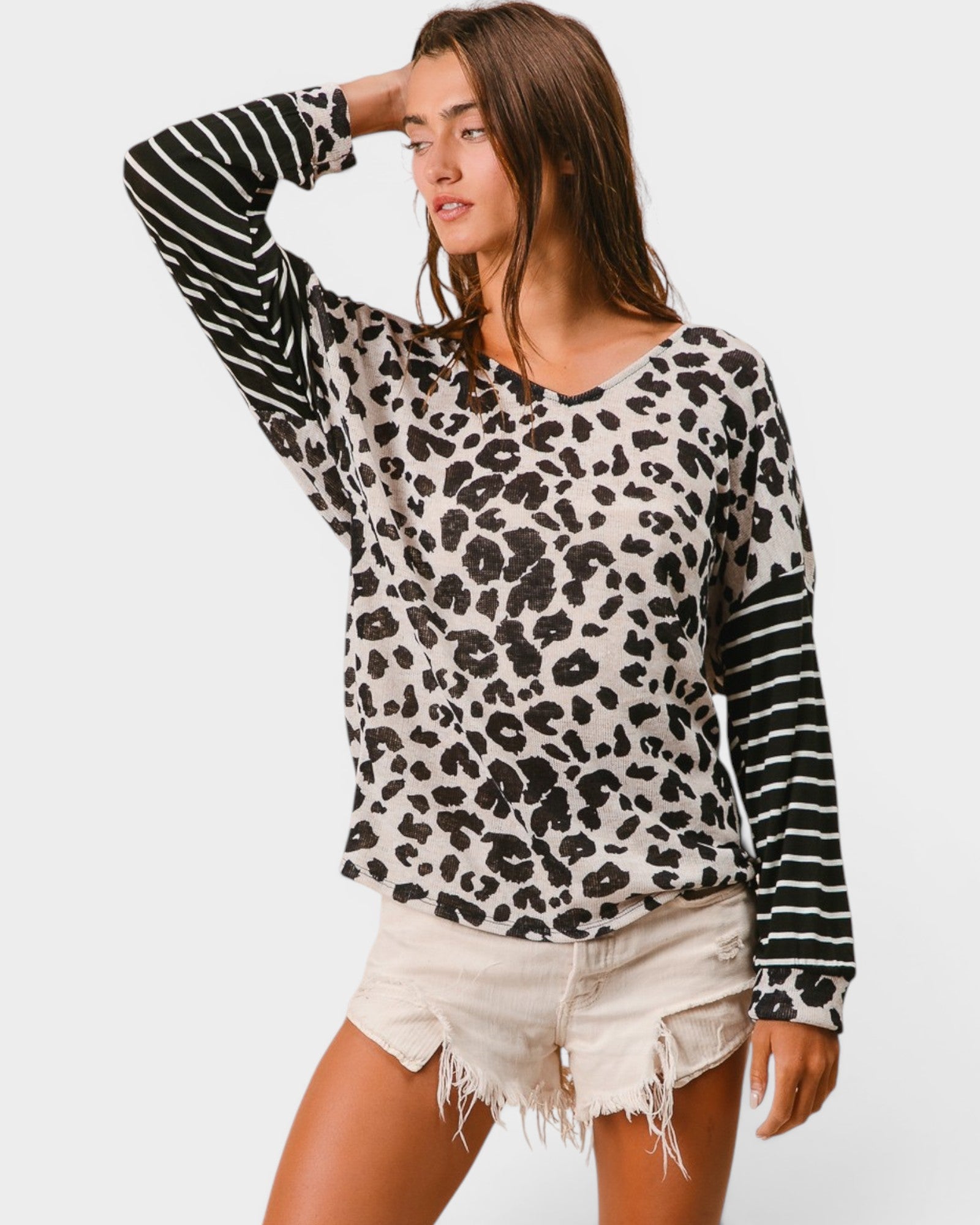 Woman wearing a leopard print sweater with black and white sleeves on a plain background