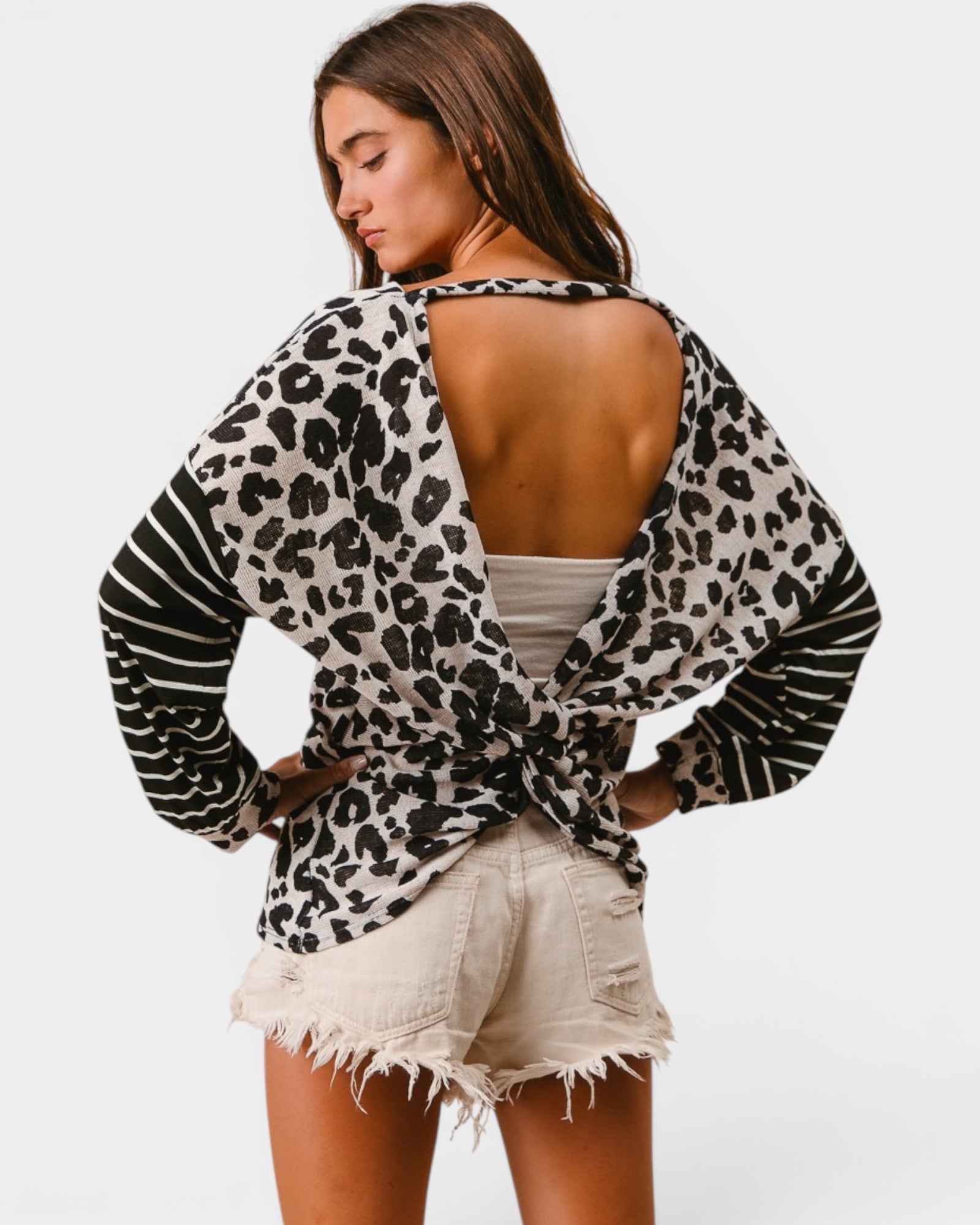 Woman wearing a leopard print open-back top and denim shorts on a white background
