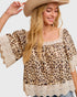 Woman wearing a leopard print top with lace details and a beige hat on a white background