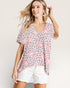 Woman wearing a patterned top with pink accents on a plain background