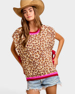 Woman wearing a leopard print top with pink trim and denim shorts on a white background