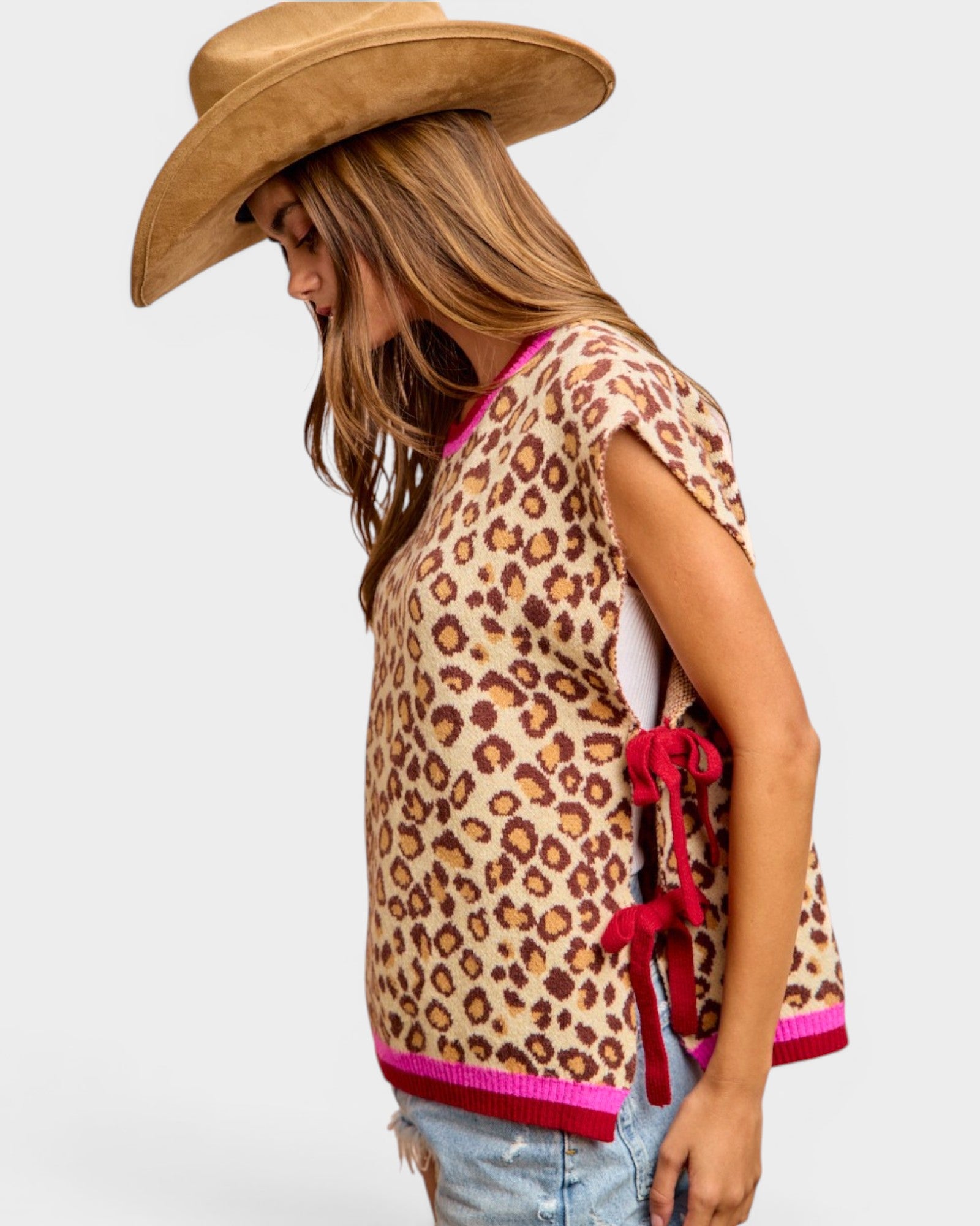 Person wearing a leopard print top with red accents and a cowboy hat on a white background