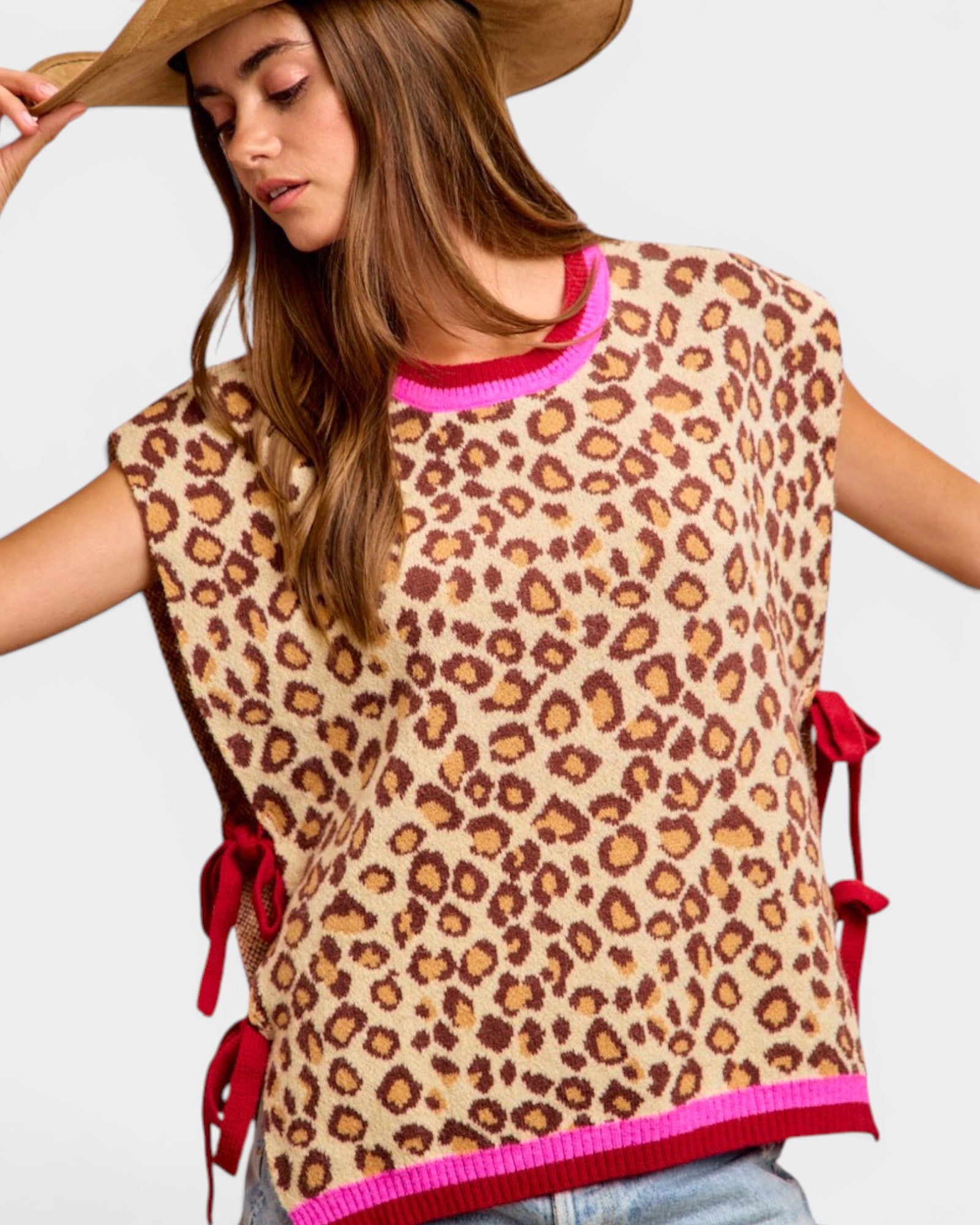 Woman wearing a leopard print top with red accents and a wide-brimmed hat on a light gray background