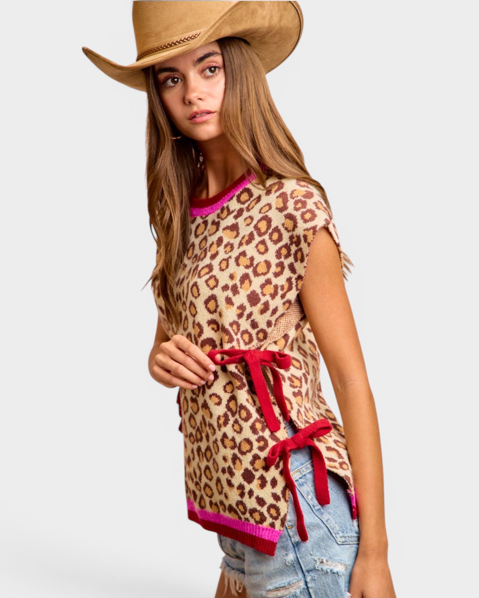 Woman wearing a leopard print top with red accents and a cowboy hat on a white background