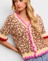 Woman wearing a leopard print cardigan with pink trim on a light gray background