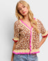 Woman wearing a leopard print cardigan with pink trim on a white background