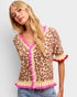 Woman wearing a leopard print cardigan with pink trim on a plain background