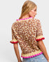 Woman wearing a leopard print top with pink trim on a plain background